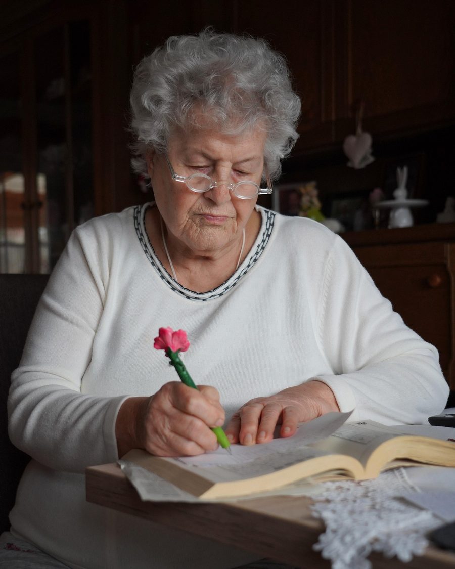 Una mujer mayor escribe en su cuaderno, con una flor entre los dedos