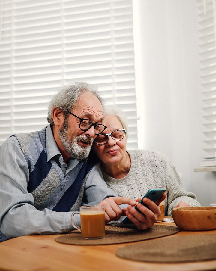 Una pareja mayor sentada a la mesa, mirando juntos el teléfono, con luz de ventana